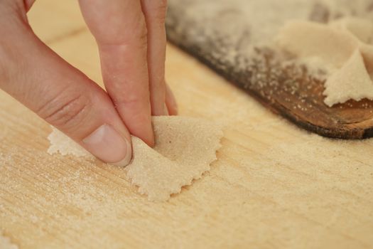 Close up macro detail of process of homemade vegan farfalle pasta with durum wheat flour. The cook kneads the dough on the wooden cutting board, traditional Italian pasta, the woman cooks the food