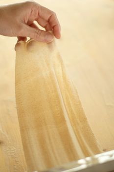 Making homemade fresh pasta: overhead top view backlit of a woman hand show the transparency of the just rolled out fresh pasta