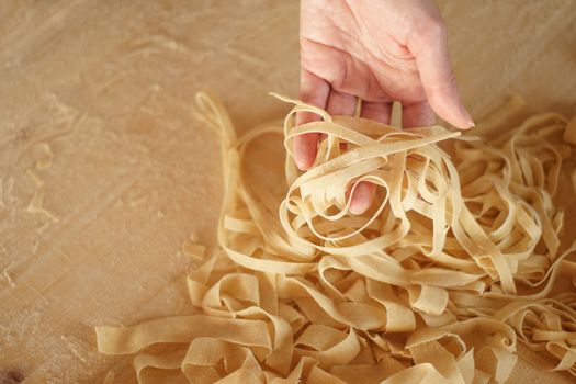 Preparing fresh homemade pasta: angle view of woman's hand pulling up some fresh fettuccine on wooden work table in natural sunlight