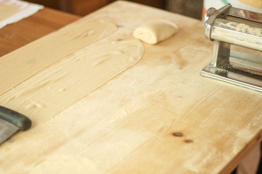 Making homemade fresh pasta: angle top view copy space of the wooden work table with flour, dough, and metal manual fresh pasta machine