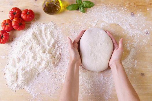 Flat lay top view of woman chef hands kneading pizza dough on wooden worktop and flour, extra virgin oil, tomatoes and basil