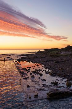 Orange and red sky with gorgeous cloud on an old abandoned sea pier in dawn or sunset with water reflections between the rocks