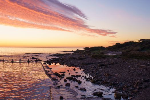 Orange and red sky with gorgeous cloud on an old abandoned sea pier in dawn or sunset with water reflections between the rocks