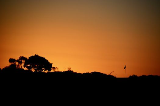 A Flagstick at a Golf Course; beautiful sunset colours and a silhouette of the golf flagstick against the evening sky.