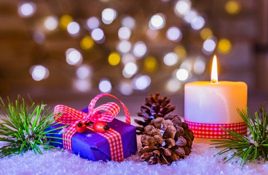 Christmas or Advent with a burning candle and gift box on snow, decorated with fir branches and pine cones