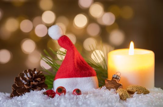 Christmas or Advent decoration with burning candle and red Santa Claus cap on snow