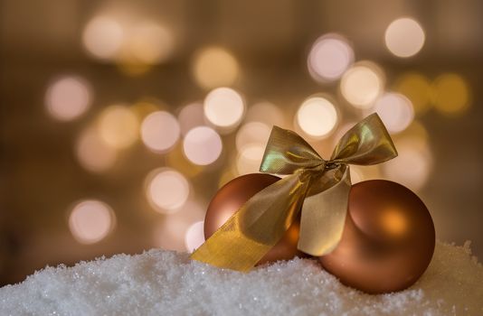 Golden Christmas ornaments with ribbon bow on snow with blurred lights background, copy space