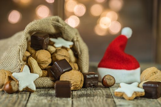 Christmas sweets and nuts food in santa claus sack and red santa hat on wooden table