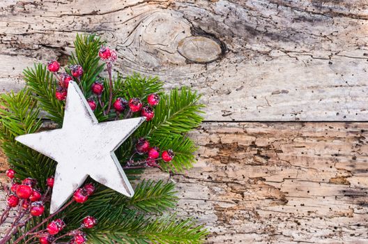 White wooden Christmas star with fir tree branch and red berries on rustic wood background