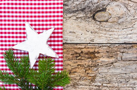 Rustic Christmas background with white wooden star, fir tree branch and red checkered fabric background