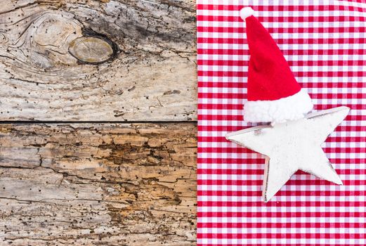 Advent and Christmas ornaments, white wooden star with red santa cap on old wood background, copy space