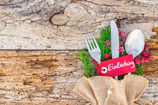 Christmas cutlery on wooden table background with tag and german text Einladung, means invitation