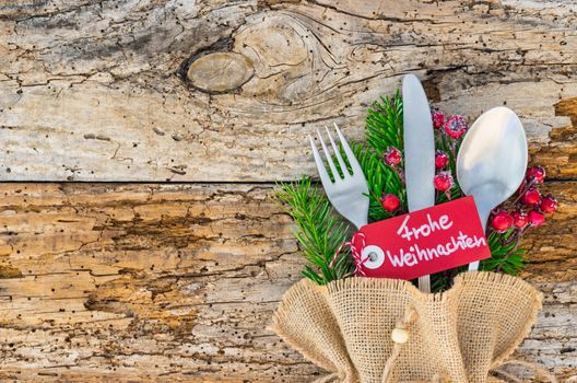 Christmas table place setting for holiday with tag and german text, Frohe Weihnachten, means Merry Christmas