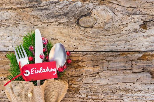 Advent or Christmas table place setting on rustic wooden background with german text tag, Einladung, means invitation