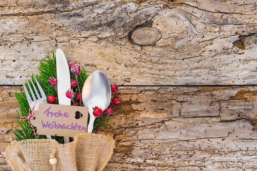 Christmas cutlery on rustic wooden table with label and german text, Frohe Weihnachten, means Merry Christmas