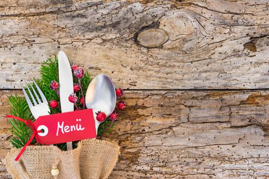 Christmas cutlery with tag and german word menue, means menu, on rustic wooden table background