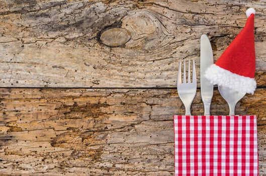 Rustic christmas dinner table place setting with santa claus hat and napkin on wood background