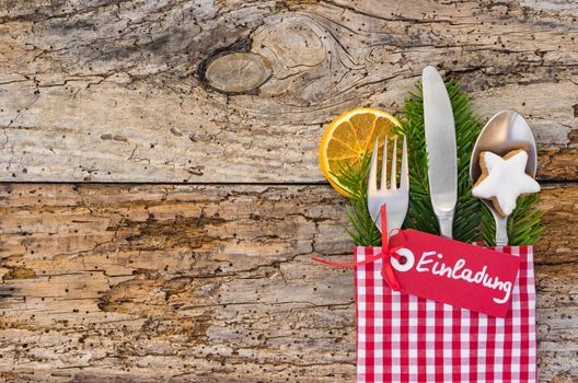 Christmas table place setting with german text tag, Einladung, means invitation, on rustic wooden background 