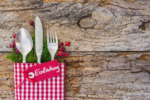 Christmas table place setting with german text tag, Einladung, means invitation, on rustic wooden background 