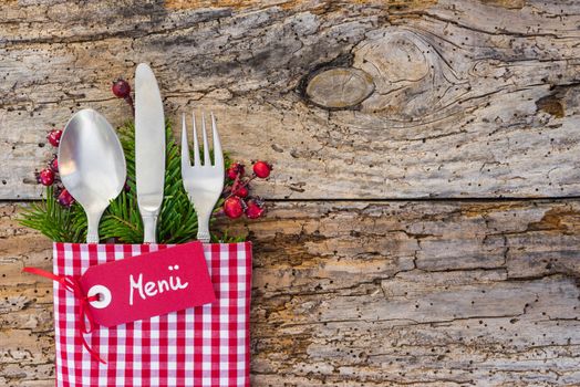 Christmas cutlery on rustic wooden table with tag and german word, Menue, means menu