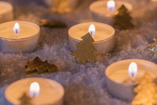 Festive christmas candle flames with golden ornaments on white snow at night