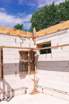 Building site of a house under construction: walls of gas concrete blocks, wooden reinforcement of windows and concrete foundation.