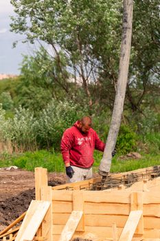 Construction worker laying cement or concrete into the foundation formwork with automatic pump. Building house foundation