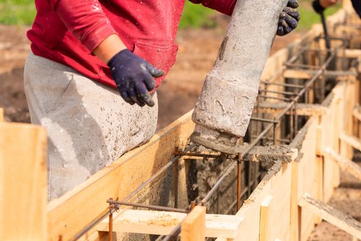 Close up of construction worker laying cement or concrete into the foundation formwork with automatic pump. Building house foundation