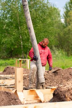 Construction worker laying cement or concrete into the foundation formwork with automatic pump. Building house foundation