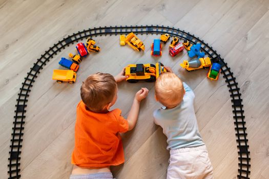 Preschool boys drawing on floor on paper, playing with educational toys - blocks, train, railroad, vehicles at home or daycare. Toys for preschool and kindergarten. Top view.