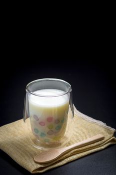 Color rice dumpling in coconut milk (Bua Loy) in transparent glass on brown table cloths on black background. Delicious Thai dessert.