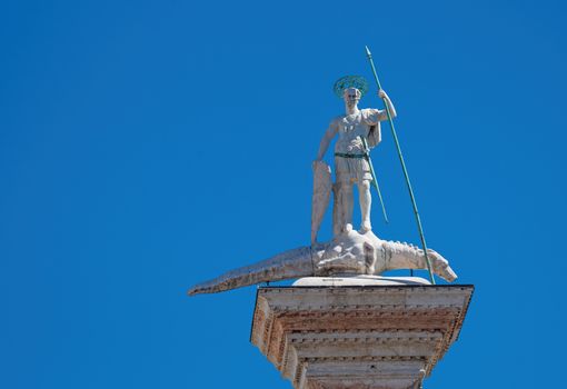 Saint Theodore medieval statue with bronze lance and shield trampling evil dragon, at the top of an ancient column erected in the 12th century in Venice
