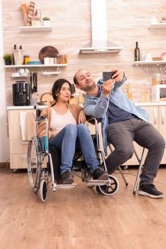 Romantic man taking selfie with disabled wife in wheelchair. Disabled paralyzed handicapped woman with walking disability integrating after an accident.