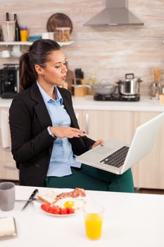 Businesswoman using a tablet for video call during breakfast. Young freelancer in the kitchen talking on a video call with her colleagues from the office, using modern internet technology