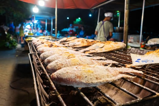 Asian food. Counter with fish in salt on the grill at a night food street market