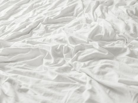 Background with white crumpled bed sheet. Creased soft linen with copy space. Unmade bed in bedroom of cozy home.