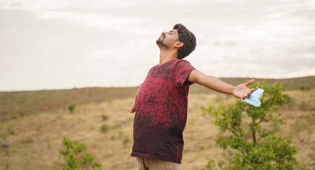 young man feeling fresh air by removing medical mask on top of mountain - concept of joy from mask obsession or came out after coronavirus or covid-19 quarantine - back to normal