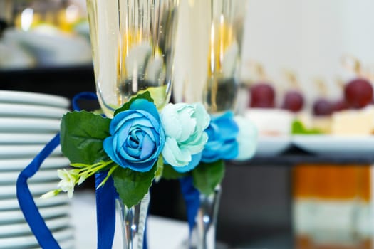 Champagne glasses are decorated with a blue ribbon with a flower. Festive banquet table for a wedding celebration