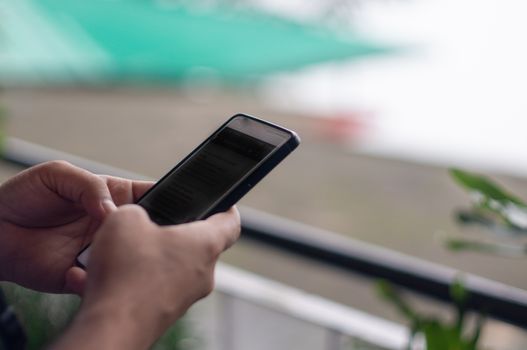 Close up shot of indian male messaging on a touchscreen mobile phone with a foggy background behind him. Shows the culture of always remaining connected even while travelling