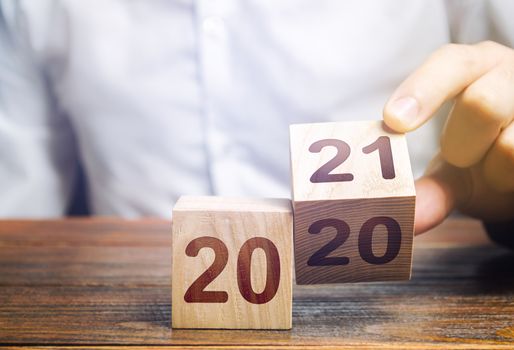 Hand flips a block changing 2020 to 2021. New year beginning. Holidays and Christmas. Trends and changes in the World. Build plans. New normal. Summing work done. Keep up with everything planned.