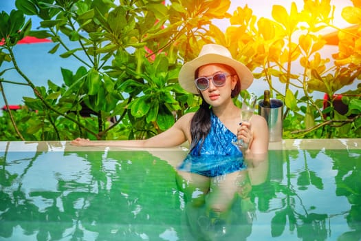 Beautiful young woman in swimming pool with a champagne in her hands