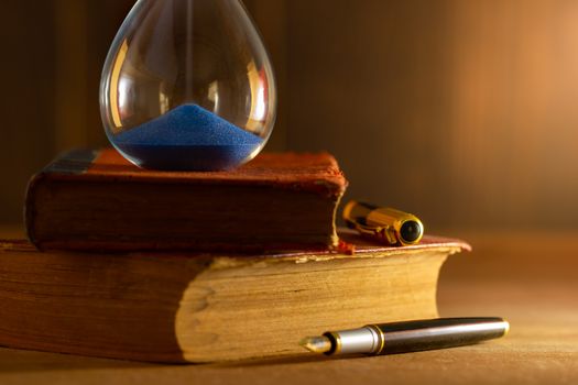 Hourglass on old book in morning light. Time of reading a book.