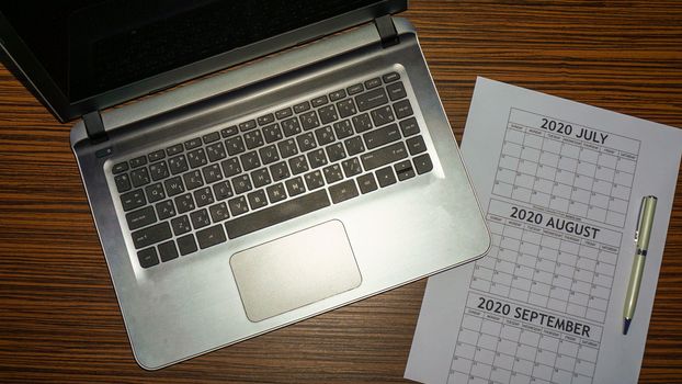 A laptop computer notebook with a pen and calendar for business or holiday planning. Planning ahead three months with a laptop and calendar.