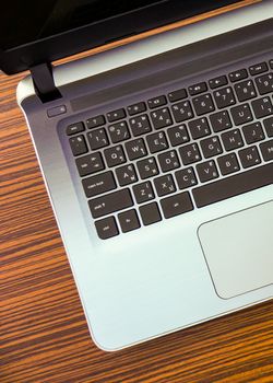 A laptop computer with English and Thai keypad on a wooden design working table.