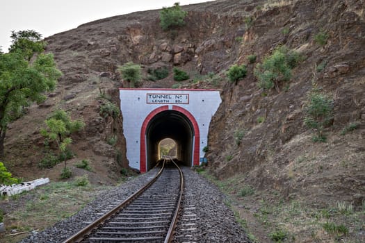 Photo of a railway track passing through a tunnel cut through a rocky hill.