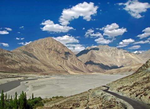 Lonely road on backdrop of beautiful mountain and blue sky on way to Diskin in Nubra valley, Ladakh, india.