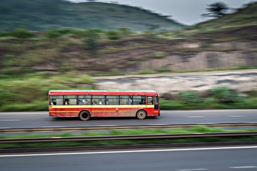 Red colored old Pune Municiapal transport local bus , speeding on highway.