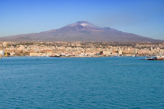 Mount Etna volcano erupting with smoke fumes dominating the Sicily coast, with Catania city and port along the Mediterranean Sea, in Italy