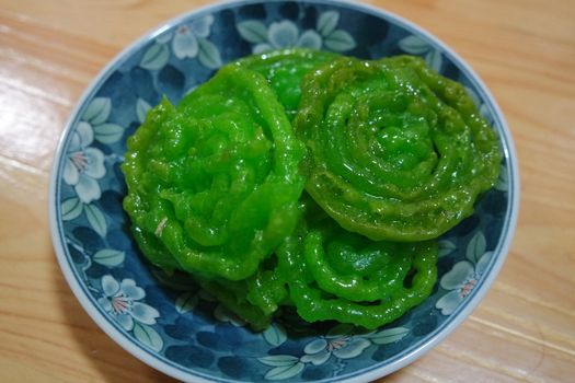 Crispy sweet Asian dessert green Jalebi cooked and served in ceramic plate, Indian sweet street food with juicy syrup, a closeup view.