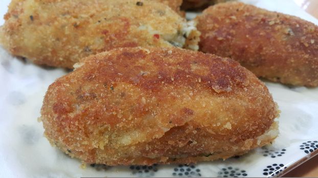 Closeup perspective view of home made spicy and delicious croquettes served in ceramic plate over wooden floor